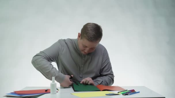 Jeune homme utilise des ciseaux pour couper un papier de couleur verte à la table dans un studio blanc — Video