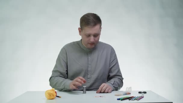 Młody człowiek rozwija metalową linię i przygotowuje ją do koralików przy stole w białym studio — Wideo stockowe