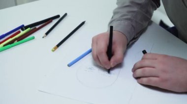 Sanatçıya yakın çekim yapmak için beyaz bir stüdyoda bir kızın yüzünü kağıda çizmek için renkli kalemler kullanır.