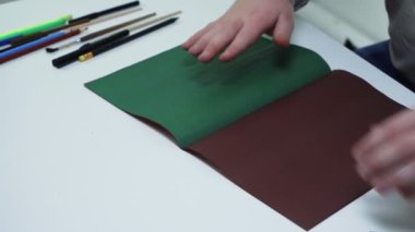 Beyaz bir stüdyodaki masada yeşil renkli bir kağıda çizgiler çizmek için üst görünüm kalem ve cetvel kullanır.