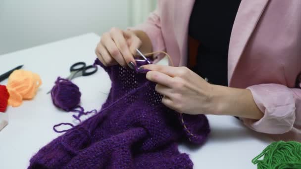 白いスタジオでテーブルの上に紫のスカーフを編む女のクローズアップ — ストック動画
