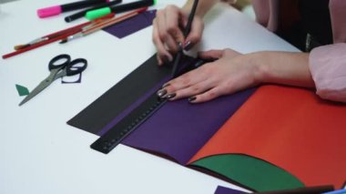 Kadının üst görünümü masadaki renk kağıdına çizgiler çizmek için kalem ve cetvel kullanır