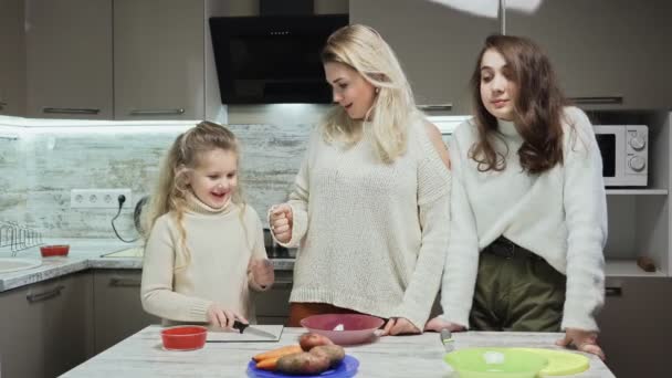 Junge Mutter kocht mit zwei Töchtern Salat in Küche. — Stockvideo