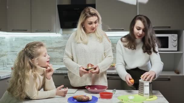 Die junge Mutter und ihre beiden Töchter kochen in der Küche Salat. Mutter putzt Kartoffeln und ihre älteste Tochter reibt Möhren — Stockvideo