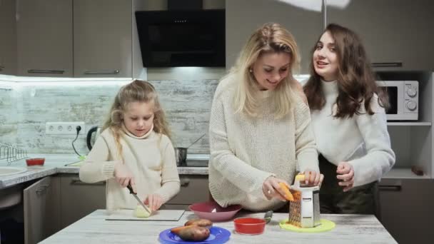 Die junge Mutter und ihre beiden Töchter kochen in der Küche Salat. Mutter hilft ihrer ältesten Tochter Möhrenraspeln — Stockvideo