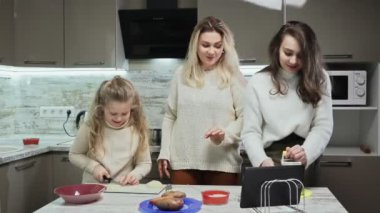 Genç anne ve iki kızı mutfakta salata pişiriyor. Annem lezzetli salata tarifi içeren tablet kullanır.