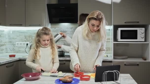 La madre giovane e due le sue figlie cucinano l'insalata a cucina. La figlia maggiore ha finito carote di grate e sua madre ha messo la carota grattugiata in piatto — Video Stock