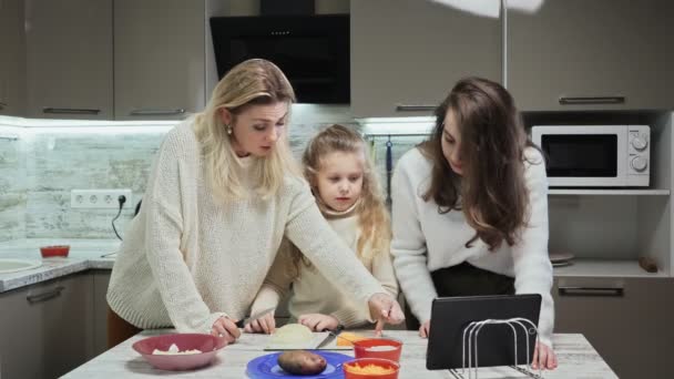 Die junge Mutter und ihre beiden Töchter kochen in der Küche Salat. Mutter und ihre Töchter schauen sich die Tablettenschnitte an — Stockvideo