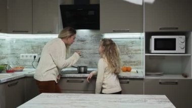 Anne ve küçük kızı çorba pişirir. Kadın tadına bakar ve başparmağını kaldırır.