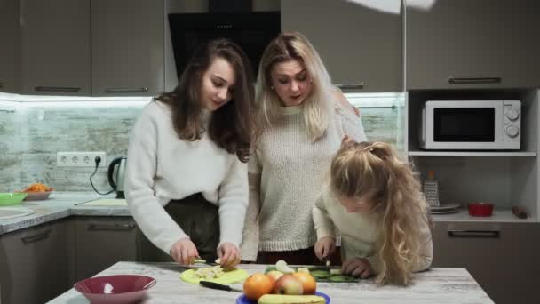 Νεαρή μητέρα και δύο κόρες της μαγειρεύουν φρουτοσαλάτα στην κουζίνα. Οι αδερφές κόβουν μπανάνες σε φρουτοσαλάτες — Αρχείο Βίντεο