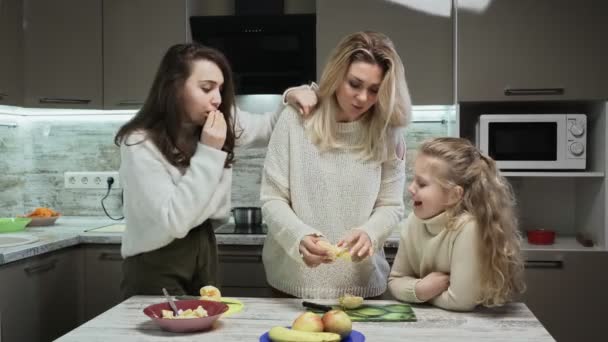 Ibu muda dan dua putrinya memasak salad buah di dapur. Ibu mengupas jeruk untuk salat buah — Stok Video