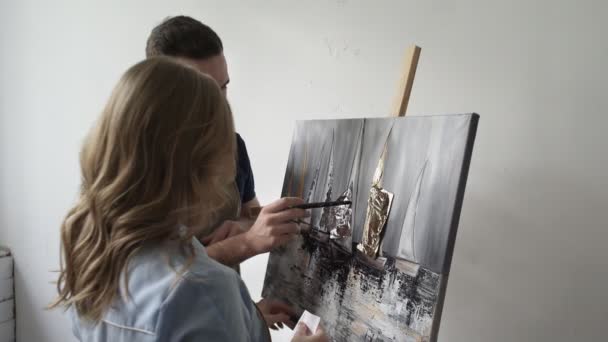 Jeune couple peint sur toile dessin image ensemble dans l'atelier d'art. Ils utilisent des couleurs et des feuilles — Video