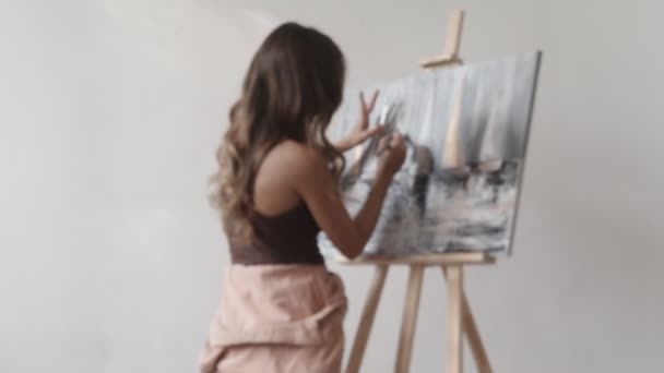 Back view of curly female artist paints picture at her workshop, creating beautiful picture, painting with colorful oils. Woman painter drawing on canvas — Stock Video