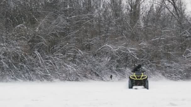 ATV Quad bike driften auf Schnee. Mann auf Quad zieht im Winter Frau in gelber Jacke auf zugefrorenem Fluss — Stockvideo