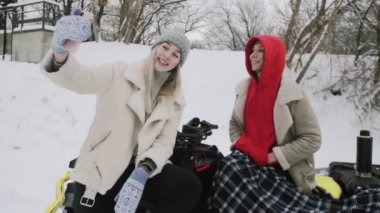 İki genç kadın, ATV Quad bisikletiyle kış ormanında poz veriyor. Kadın kız arkadaşıyla selfie çekiyor.
