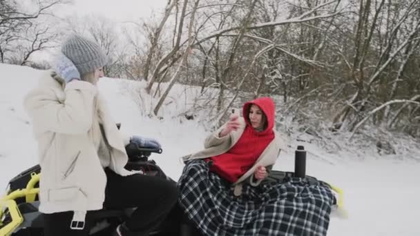 Duas mulheres jovens posando com quadriciclo ATV na floresta de inverno. Mulher tira foto de sua namorada — Vídeo de Stock