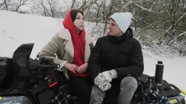 Mladý pár pózuje s ATV Quad kolo v zimním lese. Krásný muž a žena sedí na TV a mluví — Stock video