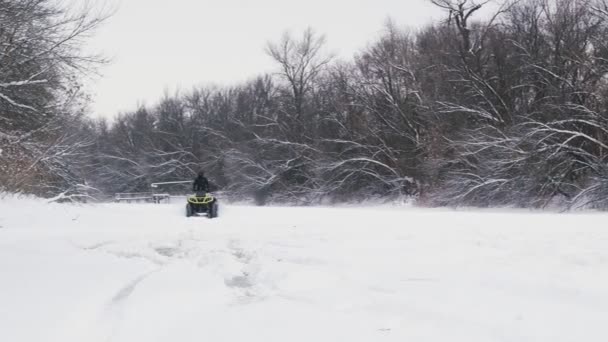 Kolo ATV Quad se vznáší na sněhu. Muž na čtyřkolce tahá ve žluté bundě žena na snowtube na zamrzlé řece v zimě — Stock video