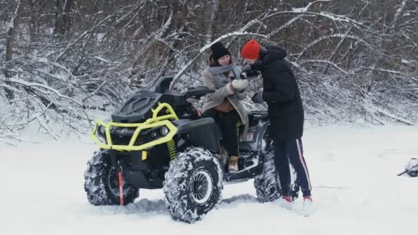 Casal jovem posando com moto ATV Quad na floresta de inverno. Jovem derrama chá de uma garrafa térmica para sua namorada — Vídeo de Stock