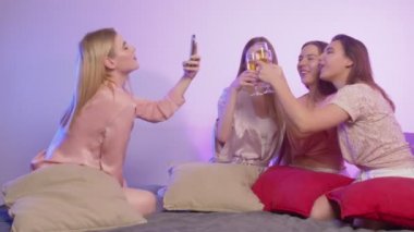 Dört mutlu, pijamalı genç kadın yatakta oturur, şarap içer ve bekarlığa veda partisinde fotoğraf çeker.