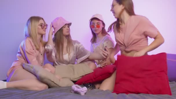 Four happy pretty young women in pajamas sits on bed and takes a silfie in sunglasses and hats at bachelorette party — Stock Video