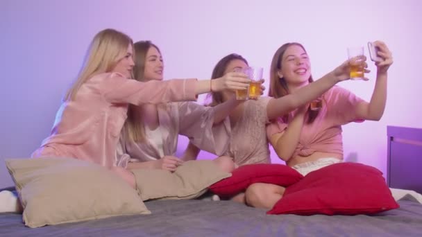Cuatro mujeres jóvenes bonitas felices en pijama y con gafas se sienta en la cama y graba video felicitación — Vídeos de Stock