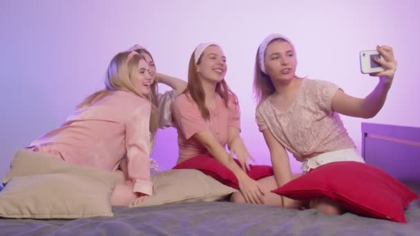 4人の幸せなかなり若い女性でパジャマはベッドの上に座って、ヘッドバンドをつけて、独身パーティーで写真を撮る — ストック動画