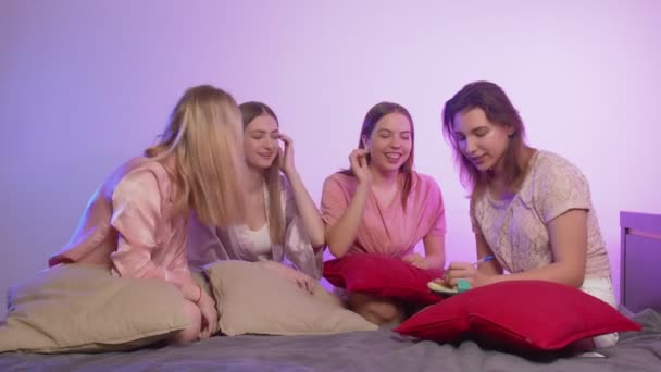 Quattro belle ragazze felici in pigiama si siedono sul letto e scrivono qualcosa in nota all'addio al nubilato. — Video Stock