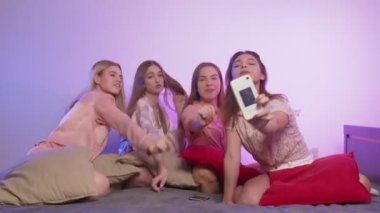 Dört mutlu, pijamalı genç kadın bekarlığa veda partisinde yatağa oturur, şarkı söyler ve telefonlarına video kaydeder.