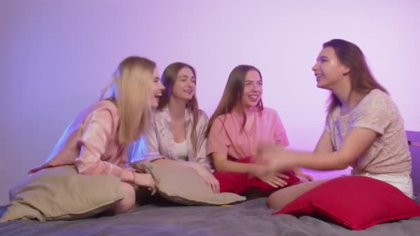 Quattro belle ragazze felici in pigiama si siedono sul letto, parlano e giocano all'addio al nubilato — Video Stock