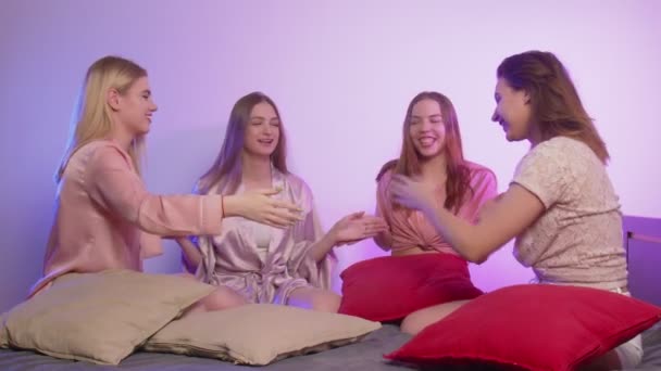 Four happy pretty young women in pajamas sits on bed, talks and plays in party at bachelorette party — Stock Video