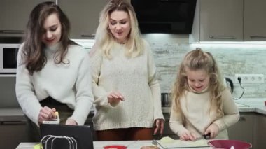 Genç anne ve iki kızı mutfakta salata pişiriyor. Annem lezzetli salata tarifi içeren tablet kullanır.