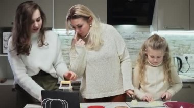 Genç anne ve iki kızı mutfakta salata pişiriyor. Büyük kızı havuç ızgarasını bitirmiş.