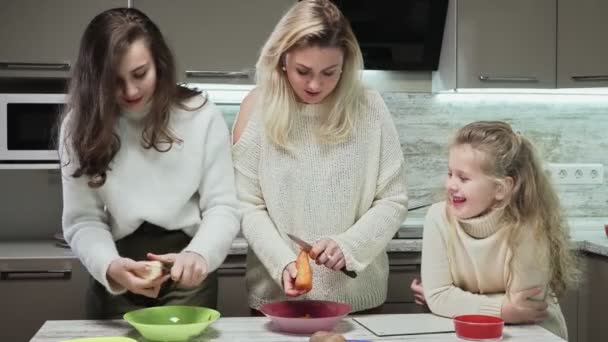 Joven madre y dos de sus hijas cocina ensalada en la cocina. Mujer e hija limpian zanahoria y papa y charlas — Vídeo de stock