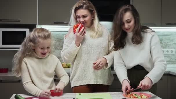 La madre giovane e due le sue figlie cucinano l'insalata a cucina. La madre taglia un pepe rosso grande — Video Stock