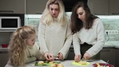 Genç anne ve iki kızı mutfakta meyve salatası pişiriyor. Anne ve kızları meyve salatası için portakal kesiyorlar.