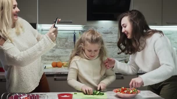 Jovem mãe tira fotos de suas filhas, enquanto cozinham salada na cozinha — Vídeo de Stock