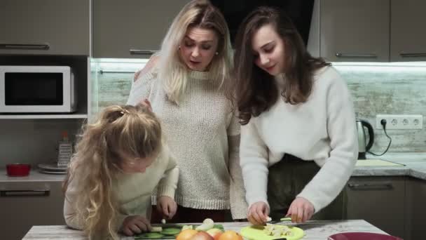 La madre giovane e due le sue figlie cucinano l'insalata di frutta a cucina. Le sorelle tagliano le banane al salato di frutta — Video Stock