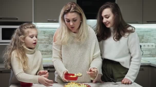 La madre giovane e due le sue figlie cucinano l'insalata di frutta a cucina. Mamma mette appena cotto satal in piatti — Video Stock
