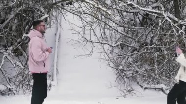 Genç bir kadın kış ormanında erkek arkadaşının fotoğrafını çekiyor.