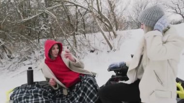 İki genç kadın, ATV Quad bisikletiyle kış ormanında poz veriyor. Kadın kız arkadaşının fotoğrafını çekiyor.
