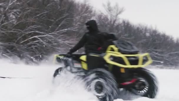 ATV Quad bicicleta a la deriva en la nieve. Hombre en quad bike tira de una mujer chaqueta amarilla en tubo de nieve en el río congelado en invierno — Vídeo de stock