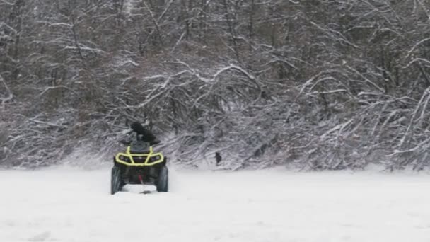 ATV Quad велосипед дрейфует по снегу. Мужчина на квадроцикле тянет в желтой куртке женщину на сноуборде на замерзшей реке зимой — стоковое видео