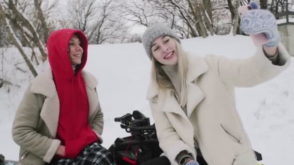 Dos mujeres jóvenes posando con ATV Quad en el bosque de invierno. Mujer toma selfies con su novia — Vídeos de Stock