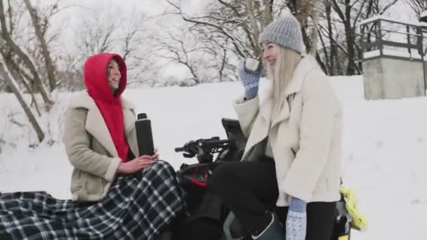 Dvě mladé ženy pózující s ATV Quad kolo v zimním lese. Šťastné ženy pijí horký čaj a mluví — Stock video