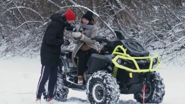 겨울 숲에서 ATV 쿼드 자전거와 포즈를 취하는 젊은 커플입니다. 젊은 남자가 자기 여자 친구에게 차를 부으다 — 비디오