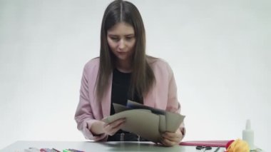 Çekici genç bir kadın, beyaz bir stüdyoda mavi bir kağıt kesmek için makas kullanıyor.