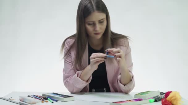 Atrakcyjna młoda kobieta wykorzystuje pastel do narysowania czegoś na białym papierze przy stole w białym studiu — Wideo stockowe