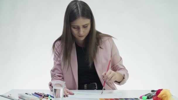 Jovem atraente desenha com aquarelas em um papel branco na mesa em um estúdio branco — Vídeo de Stock