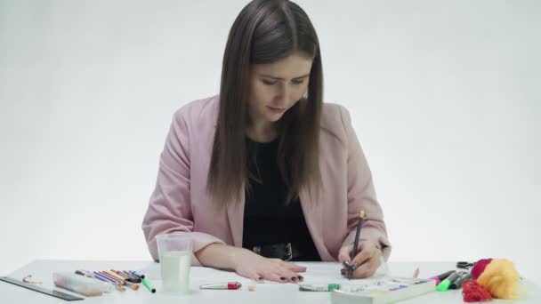 魅力的な若い女性は、白いスタジオでテーブルの上に白い紙の上に鉛筆で描きます — ストック動画